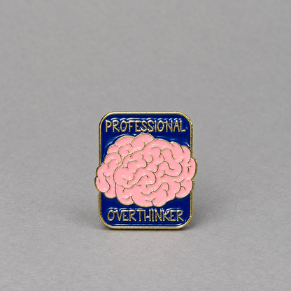 Impish Greetings Professional Over-thinker enamel pin with a pink brain design on a blue background and gold trim.