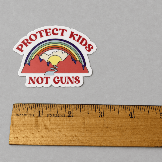 Impish Greetings Protect Kids Not Guns vinyl sticker featuring a rainbow, sun, and mountains next to a wooden ruler.