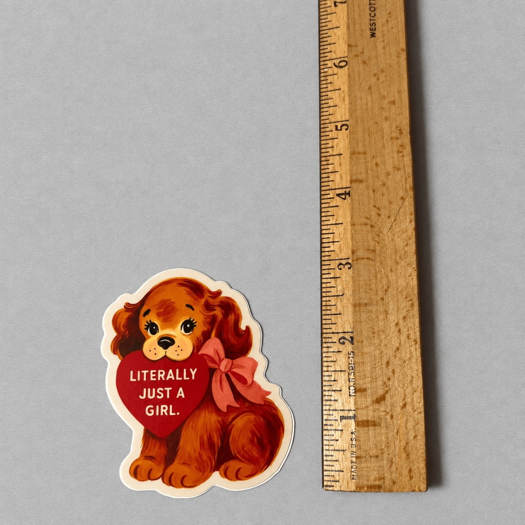 Impish Greetings Literally Just a Girl puppy sticker with a red heart and bow, shown next to a wooden ruler.