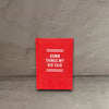 Impish Greetings Dumb Things My Kid Said tiny red hard-bound felt diary with white text on a wooden surface