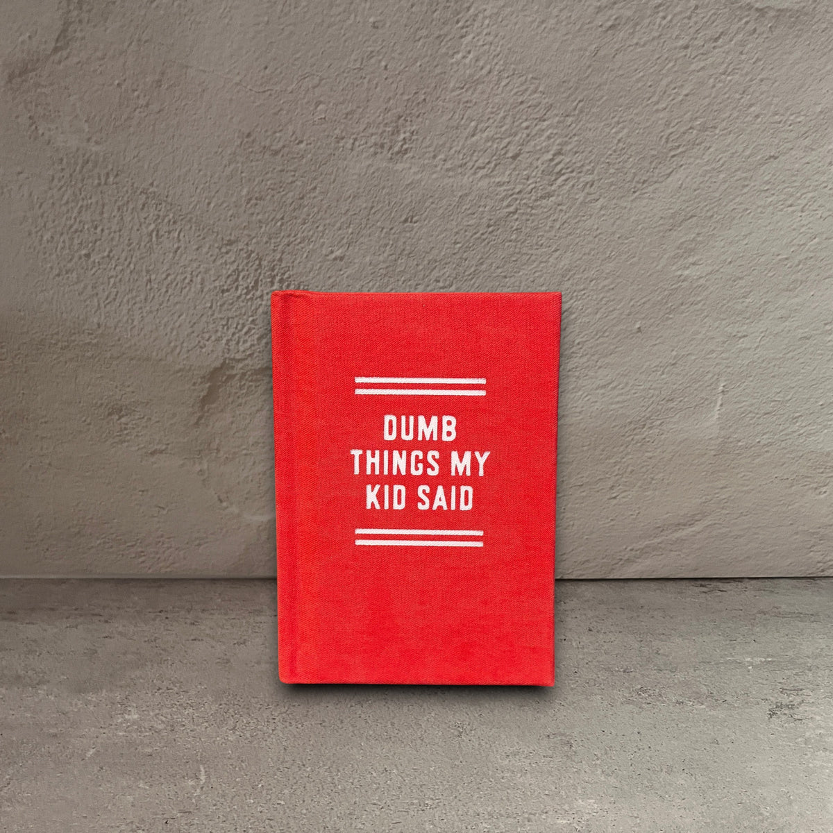 Impish Greetings Dumb Things My Kid Said tiny red hard-bound felt diary with white text on a wooden surface