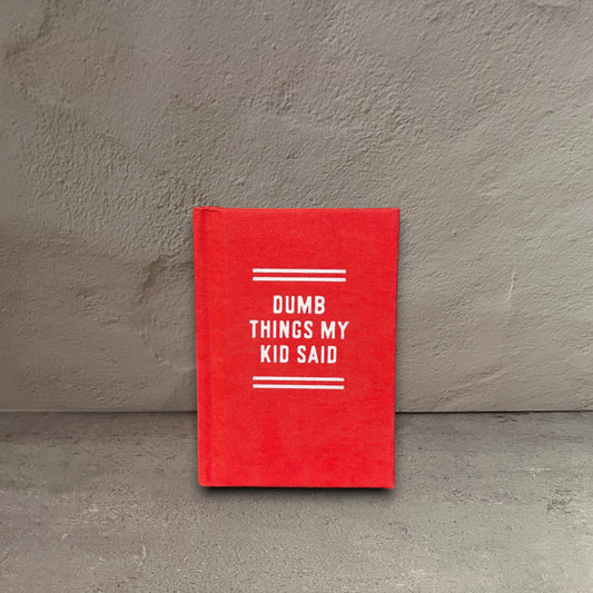 Impish Greetings Dumb Things My Kid Said tiny red hard-bound felt diary with white text on a wooden surface