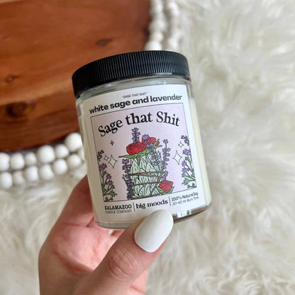 Impish Greetings Sage That Shit soy candle with white sage and lavender scent in a glass jar held in a hand