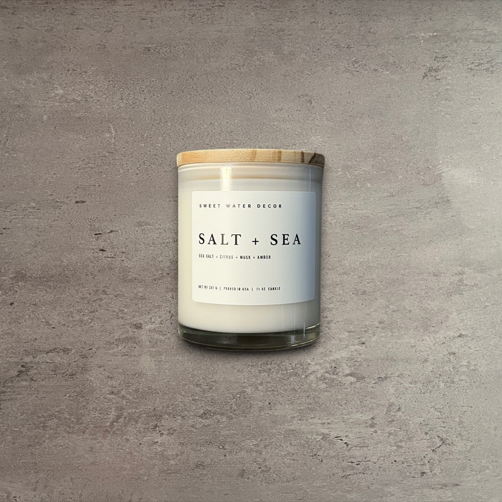 Impish Greetings Salt and Sea 11 oz soy candle in a clear glass jar with a wooden lid on a dark wood surface