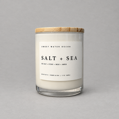 Impish Greetings Salt and Sea 11 oz soy candle in a glass jar with a wooden lid against a grey background.