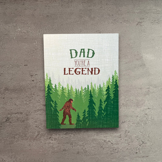 Impish Greetings Sasquatch Legend Dad card featuring a Bigfoot illustration in a forest with a brown kraft envelope.
