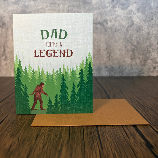 Impish Greetings Sasquatch Legend Dad card featuring a Bigfoot illustration in a forest with a brown kraft envelope.