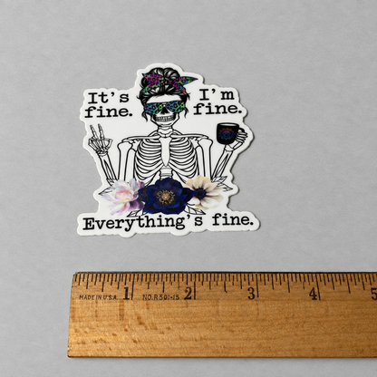 Impish Greetings vinyl sticker featuring a skeleton with a floral headband, sunglasses, and coffee, text says It's fine