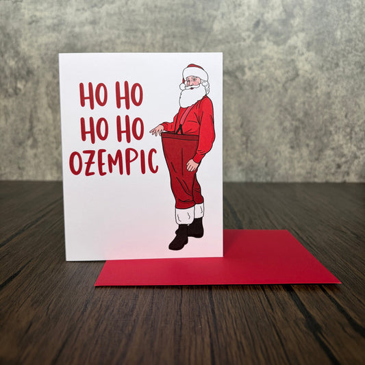 Impish Greetings Skinny Santa holiday card featuring a slim Santa in oversized red pants with red envelope.