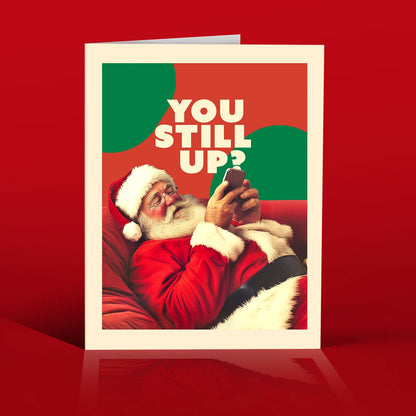 Impish Greetings Still Up? Christmas card featuring Santa Claus lounging on a red sofa while texting on his phone.