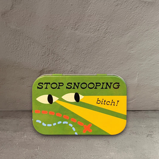 Impish Greetings green metal stash tin with Stop Snooping Bitch text and illustrated eyes on a wooden surface