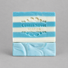 Impish Greetings Summer Cottage artisan soap bar with blue and white stripes and embossed logo on grey background