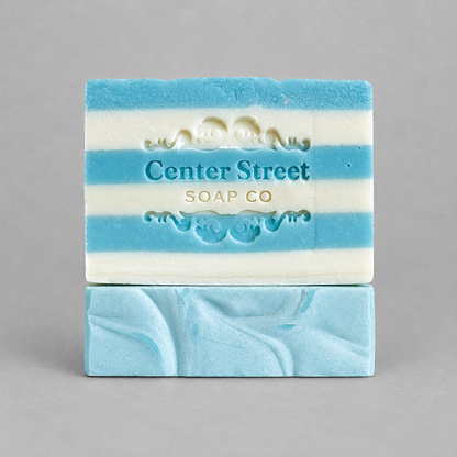 Impish Greetings Summer Cottage artisan soap bar with blue and white stripes and embossed logo on grey background