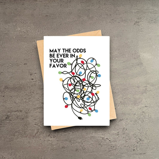 Impish Greetings funny Christmas card featuring a tangled string of colorful lights and the text May the odds be ever in your favor.