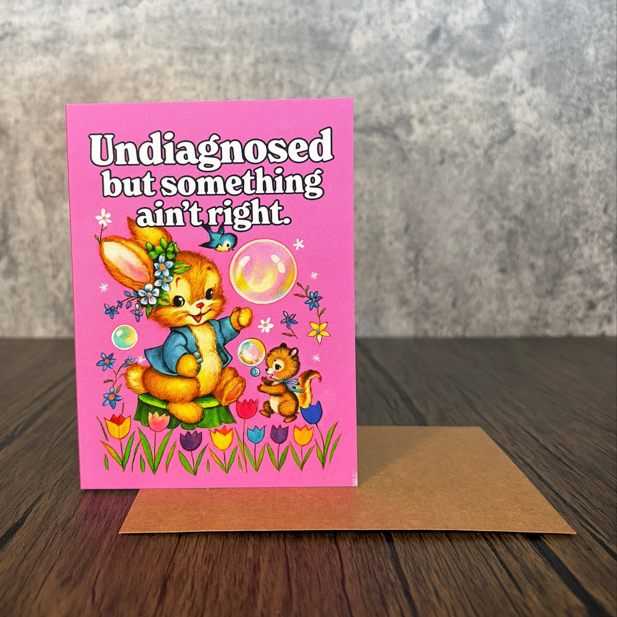 Vintage-style pink greeting card featuring a cute rabbit and squirrel blowing bubbles in a garden.