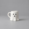 Impish Greetings white ceramic ghost-shaped coffee mug with a cute spooky face on a grey background.