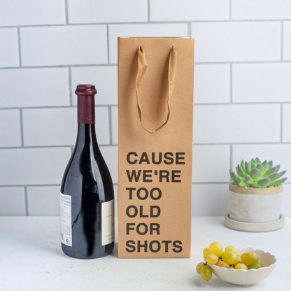 Impish Greetings kraft paper wine gift bag with Cause We're Too Old For Shots text next to a bottle of red wine