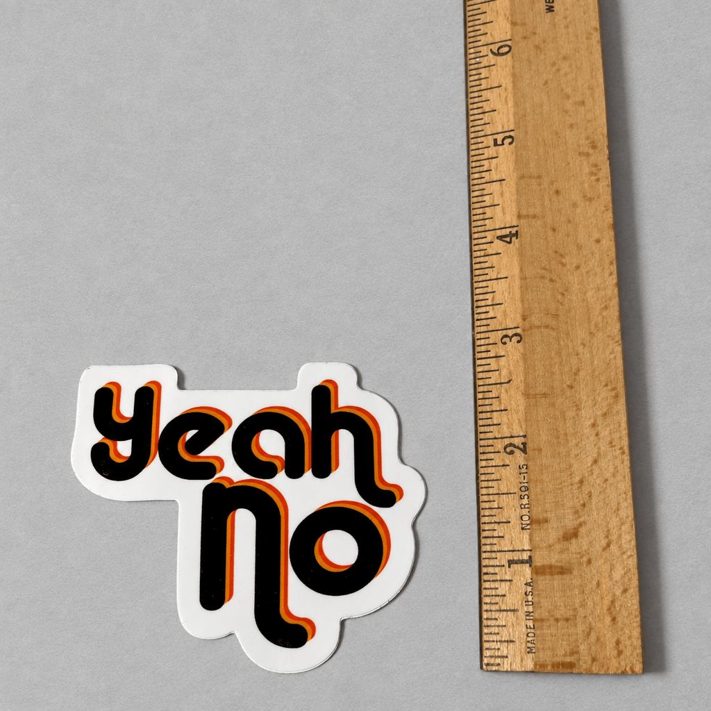 Impish Greetings Yeah No sticker with retro black and orange typography on a glossy white background next to a ruler.