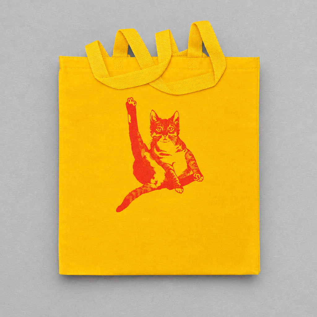 Impish Greetings yellow canvas tote bag featuring a red illustration of a cat grooming itself