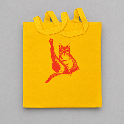 Impish Greetings yellow canvas tote bag featuring a red illustration of a cat grooming itself