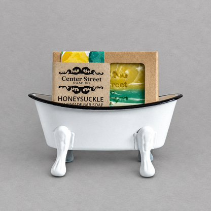 A white antique clawfoot soap holder with a white inside holding a colorful soap against a grey background