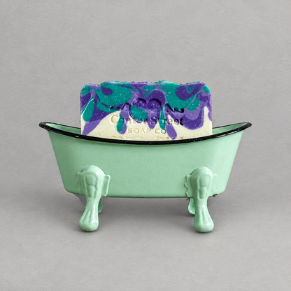A mint green antique clawfoot soap holder with a mint green inside holding a colorful soap against a grey background